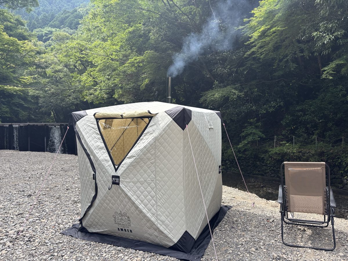 川辺で煙突から煙が上がるテントサウナ